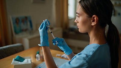 Врач-женщина готовит укол, аккуратно наполняя шприц